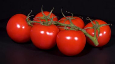 Siyah arkaplanda yeşil saplı kırmızı domateslerin yakın çekim görüntüleri.