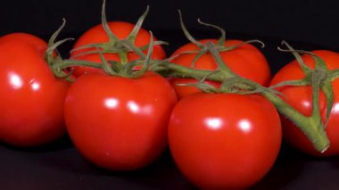 Siyah arkaplanda yeşil saplı kırmızı domateslerin yakın çekim görüntüleri.