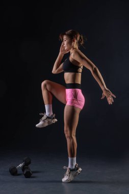 Spor anlayışı, siyah arka planda dambıllarla egzersiz yapan atletik kız.