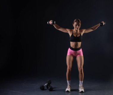 Spor anlayışı, siyah arka planda dambıllarla egzersiz yapan atletik kız.