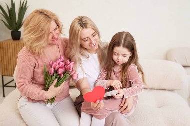 Mutlu Kadınlar Günü! Çocuğun kızı, annesine ve büyükannesine çiçek laleleri vererek onları tebrik ediyor. Büyükanne, anne ve kız gülümseyip sarılıyorlar. Aile tatili ve birlik.