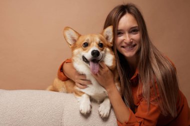 Esmer bir kız temiz bir arka planda kırmızı bir Corgi köpeğini kucaklar ve kucaklar. Hayvanlara duyulan sevgi kavramı.