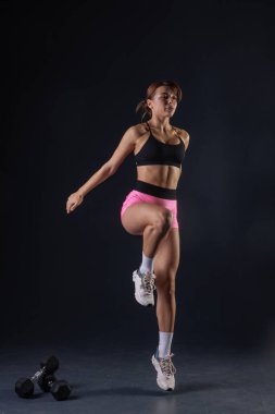 Spor anlayışı, siyah arka planda dambıllarla egzersiz yapan atletik kız.