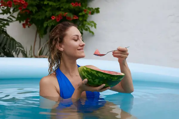 a girl in a bathing suit swims in the pool in a hot summer, a girl with a watermelon