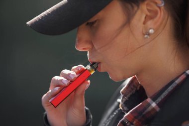 Genç bir kız karanlık bir arka planda sigara içiyor, kadınlar sokakta elektronik sigara içiyor.