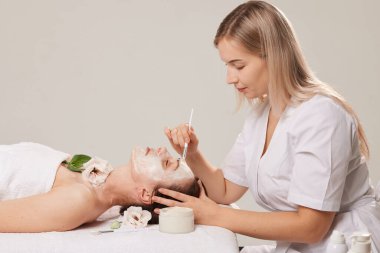 Güzellik uzmanının randevusundaki bir kızın yüzüne kremi eşit dağıtan kozmetik işlemleri için profesyonel yüz bakımı fırçası. Bakım kozmetikleri