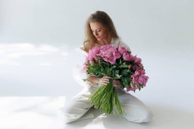 Kocaman bir buket şakayık elinde koca bir demet pembe şakayık çiçekle beyaz arka planda yüzünü ve vücudunu kaplayan bir kadın.