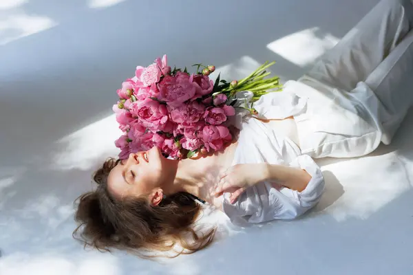 huge bouquet of peonies, Woman holding huge bunch of pink peony flowers covering her body and face on a white background