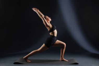 Yoga ve esneme hareketleri yapan kız, yoga ve esneme pozları koyu bir arka planda, yoga pratiği yapıyor.