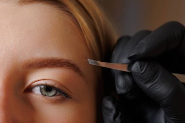 Usta kaş sanatçısı güzellik salonundaki bir kıza kaş düzeltmesi yapıyor. Kaş bakımı, kişisel bakım konsepti.