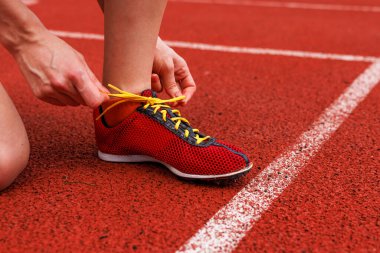 Kırmızı pabuçlarını piste bağlayan bir koşucu yarışma öncesi hazırlığa odaklanmış bir yarışa hazırlanıyor.