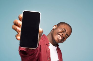 Mobil reklam. Mavi arka planda beyaz ekranlı cep telefonunu gösteren aşırı mutlu siyahi bir adam. Uygulama ya da web sitesi için bir model. Cep telefonu görüntüleme şablonu