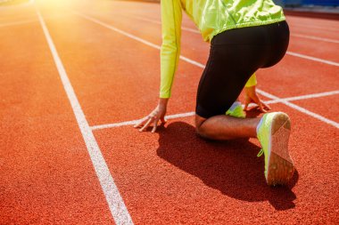 Bir koşucu başlangıç pozisyonunda, gün doğumunda bir yarış pistinde koşuya hazırlanıyor, kararlılıkla.