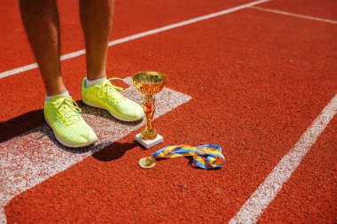 Atletizm sahasında kupa kazanan başarılı bir atlet, bacakları, bir kupa ve yakın çekim için bir madalya, sporda zafer konsepti