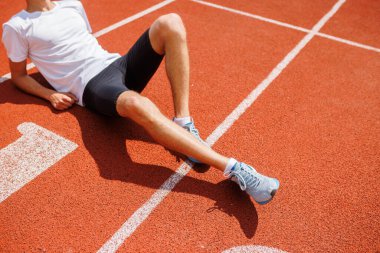 Spor kıyafetleri ve spor ayakkabıları giyerek koşu pistinde dinlenen bir sporcu..