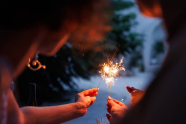 İki kişi elinde maytap tutarak neşeli bir atmosfer yaratıyor. Arka plan yeşilliklerle bulanık, kutlama havasını arttırıyor..