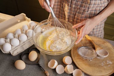 Ev mutfağının arka planında hamuru hazırlayan kadına yakın durun. Yumurta, yumurta kabuğu ve un tepsisi.