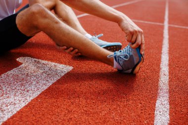 Koşu pistinde gerinen sporcu, bacaklara ve ayakkabılara odaklanıyor.
