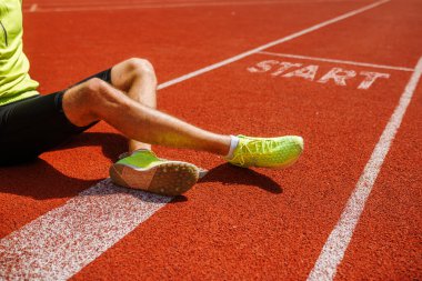 Bir koşucunun bacağının ve ayağının kırmızı bir atletizm pistinde yakın çekimi, başlama çizgisine yakın bir yerde 