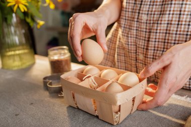 Birkaç yumurta ve mutfak arkaplanlı yumurta sepetinin üzerinde kadının elini tutarken yakın plan. Taze organik yumurta kavramı