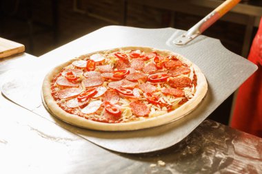 Kırmızı üniformalı bir şef peynirli ve domatesli bir pizzayı fırına koymaya hazırlanıyor..