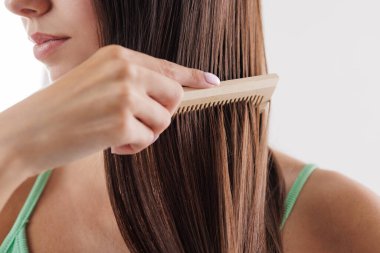 Uzun düz kahverengi saçlarını ahşap tarakla tarayan bir kadın. Saç bakımı, saç problemi