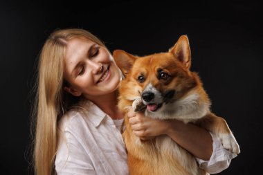 Siyah arka planda mutlu bir Corgi köpeği tutan ve kucaklayan bir kadın. Şık bir konsept. Köpekleri severim.