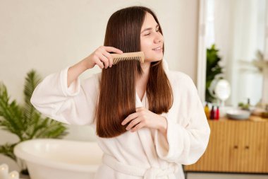 Beyaz önlüklü genç bir kız saçını evde yapıyor, saç bakım konsepti.