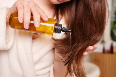 Uzun, parlak saçlarına yağ süren bir kadın. Banyo arka planı, saç bakımı...