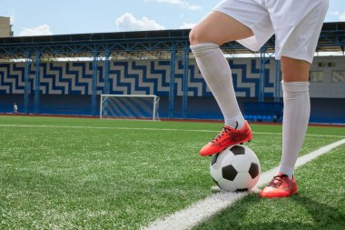 Beyaz şortlu ve kırmızı çizmeli kız futbolcu yeşil suni çim sahasında futbol topuyla ayakta duruyor. Kadınlar futbol konsepti