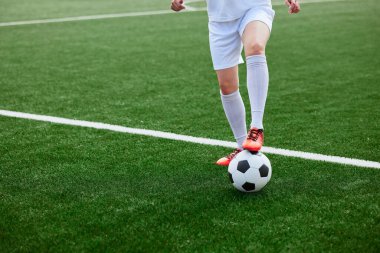 Yeşil sahada futbol topunu kontrol eden üniformalı ve kırmızı elbiseli futbolcu. futbol eğitimi