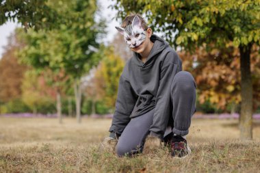 quadrobics teenager in cat mask sits on all fours in park, quadrobika subculture imitation of animal actions clipart