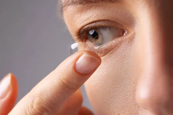 Genç bir kadın beyaz arka plan üzerinden gözüne lens takıyor. Göz giyimi, görme ve görme, göz bakımı ve sağlık, göz hekimi ve optometri konsepti. Seçici odak, kapat