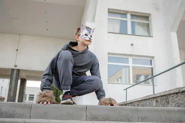 Kedi maskeli kuadrobik genci parkta dört ayak üstünde oturur, kuadrobika alt kültürü hayvan eylemlerinin taklidi