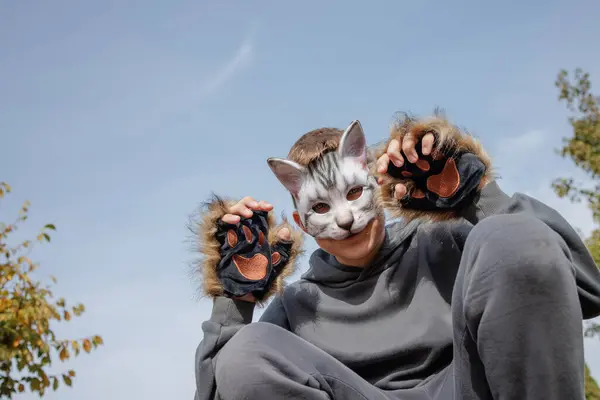 Kedi maskeli kuadrobik genci parkta dört ayak üstünde oturur, kuadrobika alt kültürü hayvan eylemlerinin taklidi