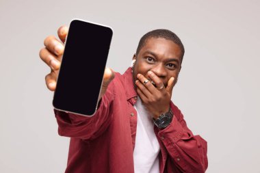 Şaşırmış Afrikalı genç adam beyaz arka planda akıllı telefon ekranı gösteriyor ve başarıya seviniyor.,