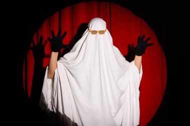 Kırmızı arka planda beyaz korkunç hayalet kostümlü adam, Cadılar Bayramı kutlaması.