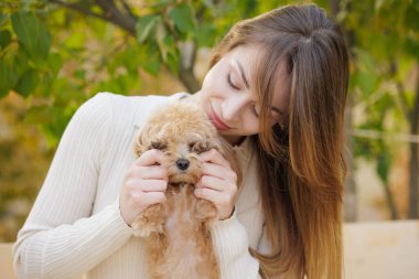 Genç ve güzel bir kadın küçük köpek oyuncağıyla oynuyor, onu tutuyor, okşuyor, sarılıyor ve neredeyse öpüyor. Muhteşem güneşli bir gün