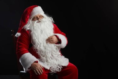 Noel Baba siyah arka planda oturur ve kameraya bakar. Noel, Yeni Yıl, Tatil Kutlaması, metin için alan