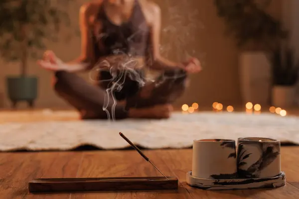 Evde yoga meditasyonu. Genç bir kız meditasyon yapıyor ve aromaterapi yapıyor. Yoga pozu vermiş bulanık bir kızın arka planında sigara aromalı raflara yakın çekim yapıyor.