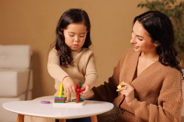 Asyalı güzel anne evde kızıyla eğitim oyunu oynuyor. Çekici bir kadın ebeveyn, boş zamanlarını küçük kız çocuğuyla geçirir. Çocukların oyuncaklarıyla vakit geçirir ve yeteneklerini geliştirir..
