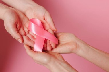 Renkli arka planda pembe farkındalık kurdelesi olan kadın eller, yakın plan. Göğüs kanseri konsepti, hayır işi sağlık hizmetleri yardım ve destek