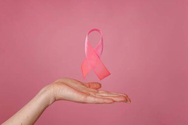 Renkli arka planda pembe kurdeleli kadın eller, yakın plan. Göğüs kanseri farkındalığı kavramı, göğüs kanseri farkındalığını sembolize eden pembe kurdele.
