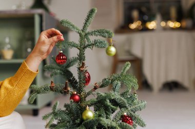 Sarı kazaklı bir kadın ev ortamında küçük bir Noel ağacını oyuncaklarla süslüyor. Mutlu Noeller.