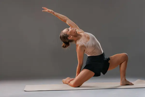 Paspasın üzerinde yoga pozu veren bir kadın esneklik ve güç gösterisi yapıyor. Arkaplan tarafsız, duruşunu ve duruşunu vurguluyor..