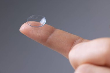 Vizyon düzeltme ve bakım konsepti. Gri arkaplanda parmak üzerine kontak lensin yakın plan görüntüsü.