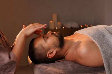 Kadın masör, masaj salonunun sıcak atmosferinde erkeğe yüz masajı yapıyor.
