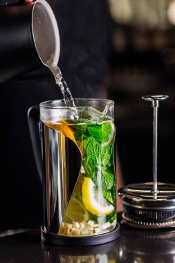 Limonlu, zencefilli ve naneli vitaminli çay şeffaf bir çaydanlıkta koyu bir arka planda.