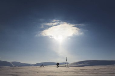 Berrak mavi gökyüzünün ve ufukta batmakta olan güneşin altında arka planda karla kaplı, sakin bir kuzey kutbu kış manzarası..