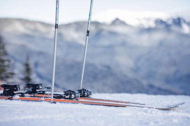 Karlı bir dağ yamacında arka planda bulanık bir dağ sırası olan bir çift kayak ve kutup..